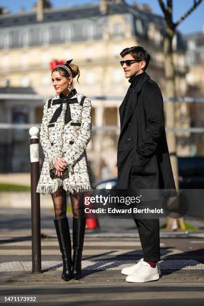 Olivia Palermo wears a black tulle knot hair clip, a pink velvet headband, diamonds and white pearls pendant earrings, a white with black embroidered...