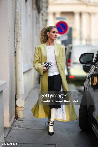 Emili Sindlev wears diamonds earrings, a silver chain necklace, a white tank-top from Miu Miu , a pale green shiny leather long coat, a black and...