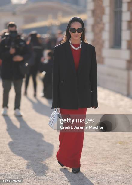 Fashion week guest seen wearing a long red dress, a pearl necklace, an oversized black blazer, black shades, a silver leather bag and black heels...