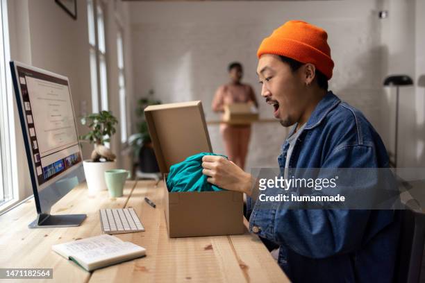 young asian man excited to receive his online order and open the package - textile for delivery stock pictures, royalty-free photos & images