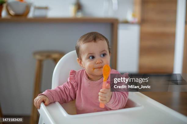 niña comiendo en silla alta - cuchara fotografías e imágenes de stock