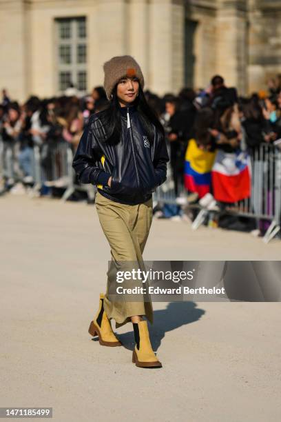 Yoyo Cao wears a brown fluffy beanie from Loewe, silver earrings, a black shiny leather with embroidered white logo pattern zipper bomber coat from...