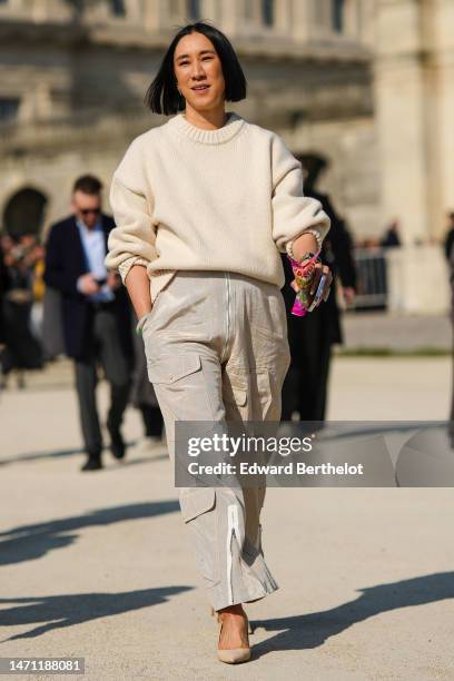 Eva Chen wears a white latte wool pullover, beige shiny satin cargo pants, gold bracelets, a gold watch, beige shiny leather pointed pumps heels...