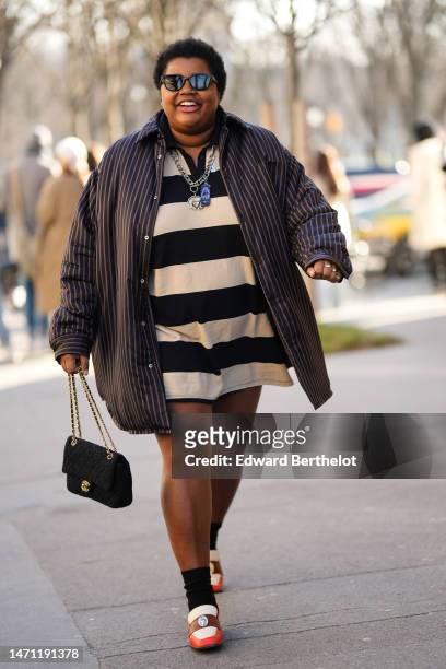 Gabriella Karefa-Johnson wears black sunglasses, a beige and black large striped print pattern polo shirt short dress, a dark brown striped print...