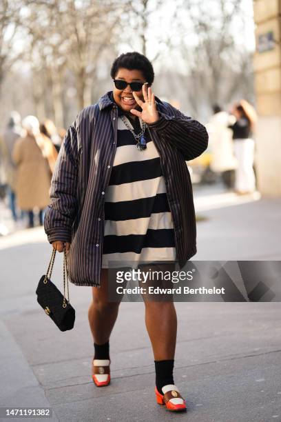 Gabriella Karefa-Johnson wears black sunglasses, a beige and black large striped print pattern polo shirt short dress, a dark brown striped print...