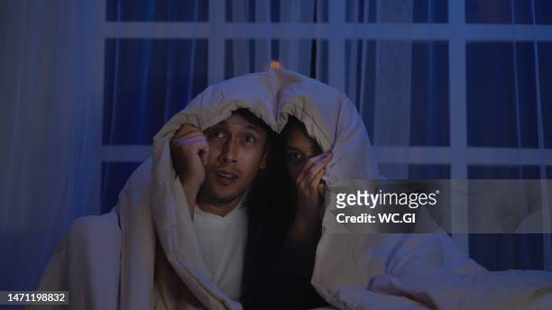 asian couple watch horror movies on the bed with blanket to cover their heads - escandalo tv fotografías e imágenes de stock
