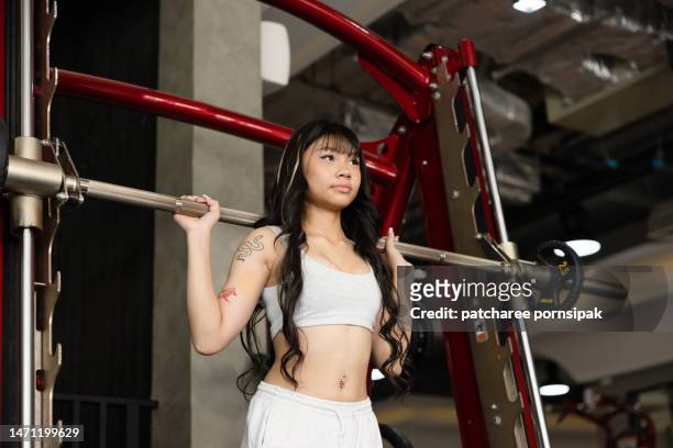 teenage girl playing with barbell machine workout in the gym to have a good health shape - girl bums 個照片及圖片檔