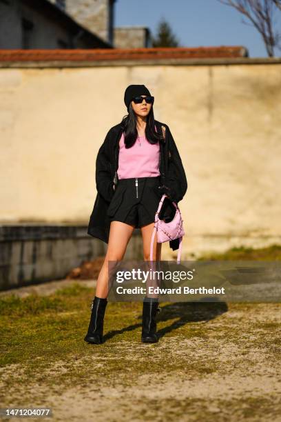 Susanna Lau wears a black wool beanie, black squared sunglasses, a pink tank-top from Givenchy, a black braided wool oversized cardigan, a black...