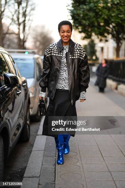 Tamu McPherson wears gold micro earrings, a black and white zebra print pattern t-shirt, a black shiny leather with embroidered silver nailed /...