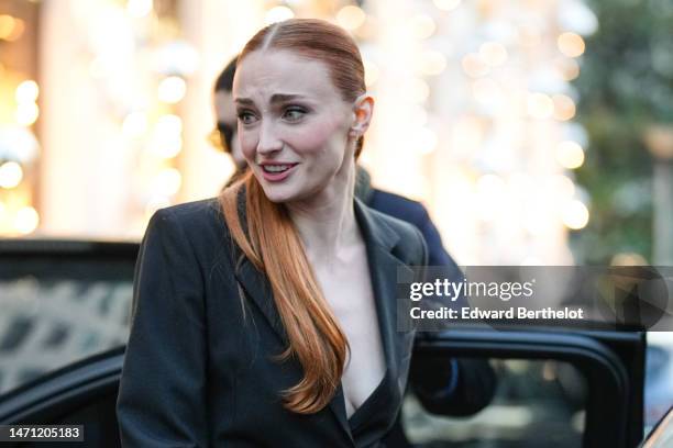 Sophie Turner wears gold earrings, a black blazer jacket, black shiny varnisged leather pants, a white shiny leather handbag, outside the LVMH...