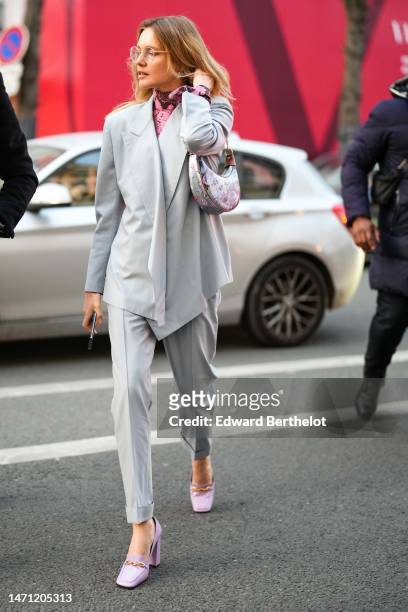 Natalia Vodianova wears gold glasses, a pink print pattern turtleneck pullover, a pale gray wrap blazer jacket, matching pale gray suit pants, a...