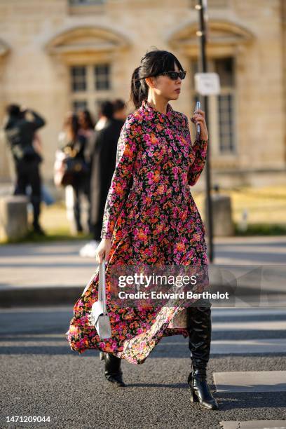 Susanna Lau wears black sunglasses, a black with neon orange / pink / green / purple flower print pattern shirt neck / long sleeves / long dress, a...