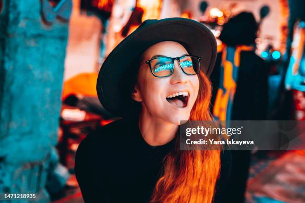 young pretty hipster woman in glasses and hat is dancing in neon lights - sombrero de fiesta fotografías e imágenes de stock