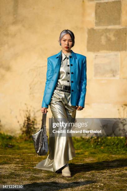 Guest wears blue earrings, a white high neck t-shirt, a silver shiny leather buttoned jacket, a blue shiny leather buttoned blazer jacket, a black...