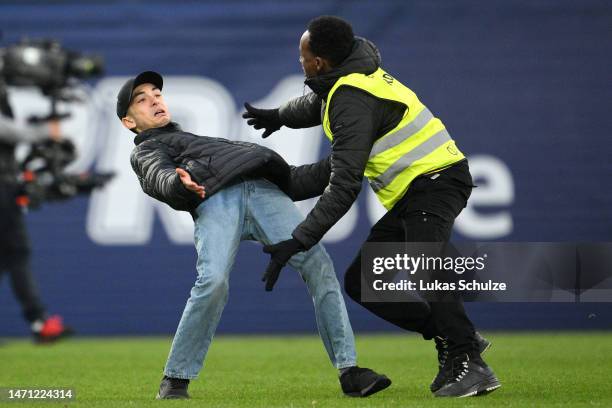 Streaker on the pitch is detained by security following during the Bundesliga match between 1. FSV Mainz 05 and TSG Hoffenheim at MEWA Arena on March...