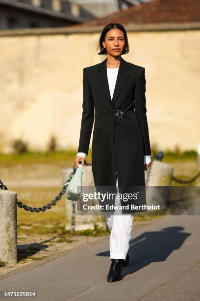 Guest wears a white t-shirt, a black shoulder-pads long coat with a silver buckle logo belt from Givenchy, white denim large pants, a pale green...