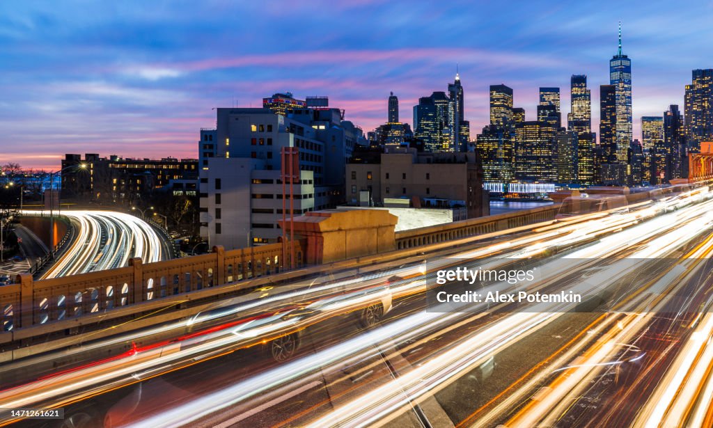 Illuminated Manhattan, seen from the Brooklyn Bridge with busy traffic and Brooklyn-Queens Expressway. Blurred motion effect. Extra-large, high-resolution, stitched panorama.