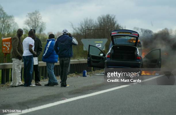 Group of men stand on the hard shoulder besides their car which has caught fire as they wait for the emergency services to arrive on the M4 motorway...