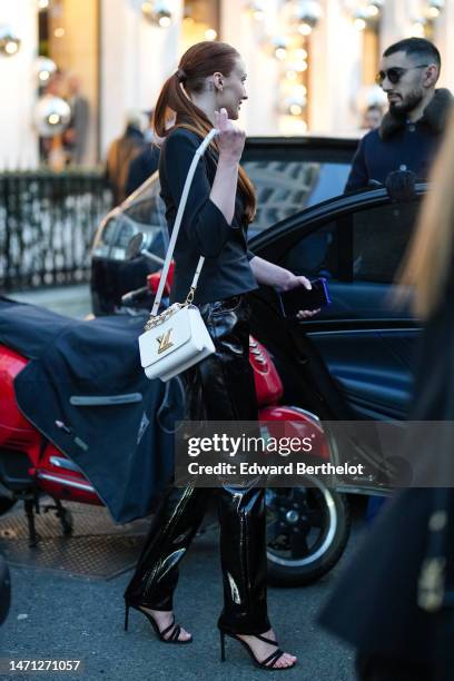 Sophie Turner wears gold earrings, a black blazer jacket, black shiny varnisged leather pants, a white shiny leather handbag from Louis Vuitton,...