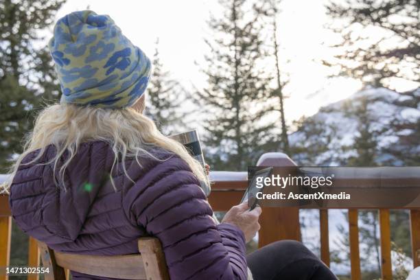 woman uses e-reader and enjoys hot drink on cabin veranda - canmore stockfoto's en -beelden
