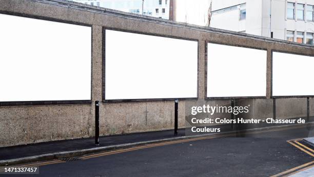 four white and empty advertising panels on a weathered wall with sidewalk and street in london, england, united kingdom - poster wall stockfoto's en -beelden