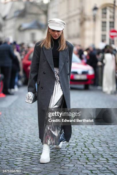 Guest wears a white latte felt wool with embroidered rhinestones pattern cap, a black turtleneck wool pullover, a dark gray wool long coat, a silver...