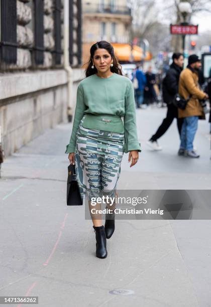 Guest wears green jumper, black bag, skirt with print, black ankle boots outside Hermes during Paris Fashion Week - Womenswear Fall Winter 2023 2024...