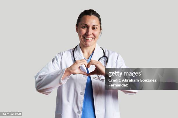 female doctor looking at the camera making a heart gesture with both hands in a studio shot - doctor attitude stock pictures, royalty-free photos & images