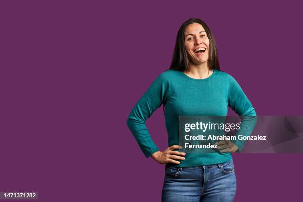 woman standing while she has her hands on her waist and looks camera against a purple background - mano sobre la cadera fotografías e imágenes de stock
