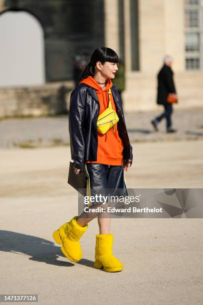 Guest wears a black earring, black and silver necklaces, a neon orange hoodie sweater from Loewe, a yellow shiny leather Puzzle fanny pack bag from...