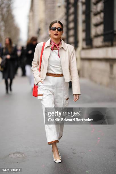 Paola Alberdi wears black sunglasses, a white and red print pattern silk scarf, a white shoulder-off / denim wide legs pants with a camel belt...