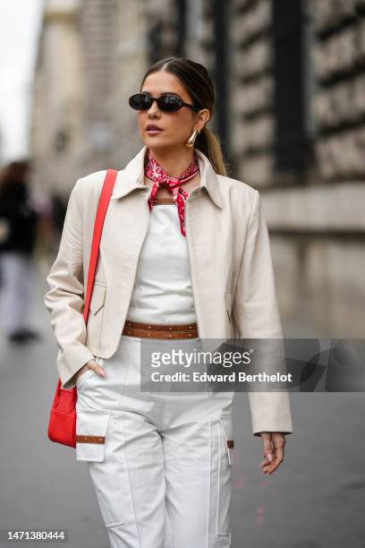 Paola Alberdi wears black sunglasses, a white and red print pattern silk scarf, a white shoulder-off / denim wide legs pants with a camel belt /...