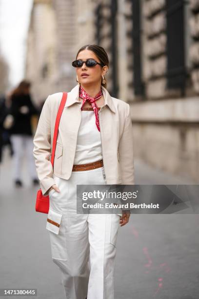 Paola Alberdi wears black sunglasses, a white and red print pattern silk scarf, a white shoulder-off / denim wide legs pants with a camel belt /...