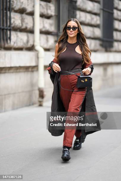 Tamara Kalinic wears black butterfly sunglasses, diamond earrings, a dark brown and black borders halter-neck tank-top, a black with camel striped...