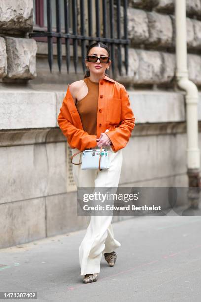 Alexandra Pereira wears black and brown sunglasses, gold and diamonds earrings, a camel halter-neck tank-top from Hermes, an orange shiny grained...