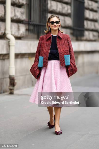 Guest wears black sunglasses, a red rose flower and crystals pendant earrings, a white t-shirt, a black wool pullover, a red and black small striped...