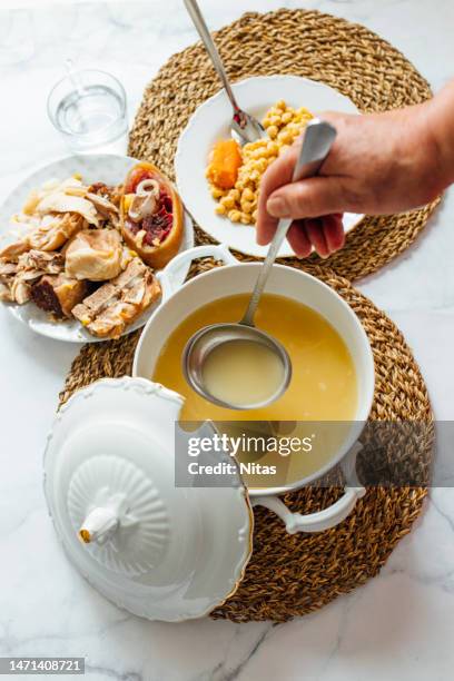 top view of senior mature woman hand serving cocido. cocido is a stew with chickpeas, meats and soup with noodles typical madrilenian food and dish very popular in spain on winter days - camel colored stock-fotos und bilder