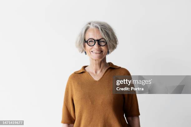 smiling senior woman standing against white wall - bovenlichaam stockfoto's en -beelden