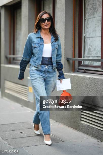 Guest wears black large futurist sunglasses, a white V-neck tank-top, a blue denim with navy blue embroidered long sleeves jacket, matching double...
