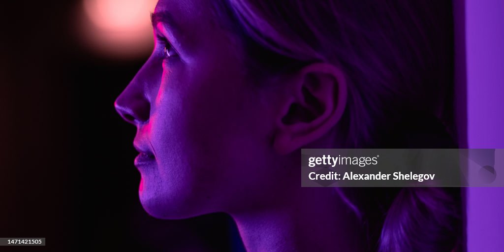 Female portrait in neon color indoors, person with purple, blue, red and pink light. Woman photo, lifestyle concept photography with multi coloured lights and colors.