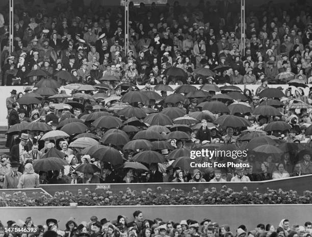 Spectators, some sheltering beneath umbrellas, watching the Coronation procession of Elizabeth II in Westminster, London, England, 2nd June 1953. The...