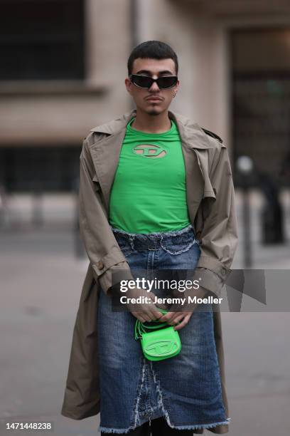 Fashion week guest seen wearing black shades, a neon green shirt by Diesel and a matching neon green minibag by Diesel, e beige trench coat, a jeans...