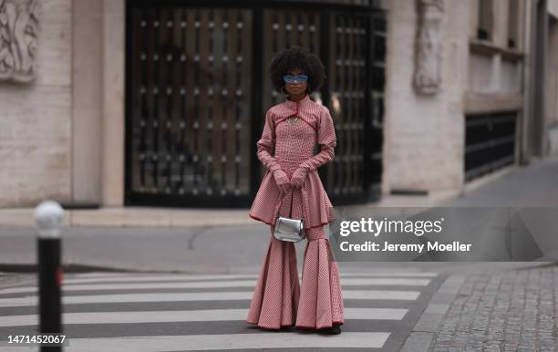 Fashion week guest seen wearing a red and white checked look with a bolero, gloves, a corsage and wide leg pants, a silver bag and blue shades before...