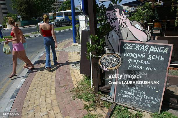 Tourists pass by a menu written in Russian placed outside a restaurant in Limassol 22 August 2003.