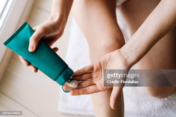 woman sitting by the window on the bathroom floor, massaging body cream. care procedures, spa, relaxation - crema hidratante fotografías e imágenes de stock