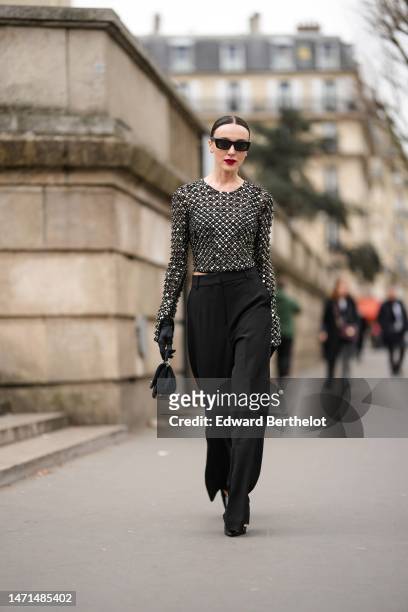 Mary Leest wears black sunglasses, diamond earrings, a black tulle with embroidered silver and black pearls pattern long sleeves top, black satin /...