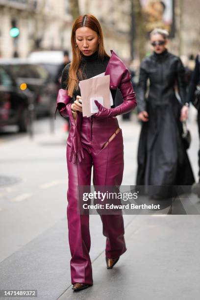 Guest wears burgundy futurist sunglasses, a black turtleneck pullover, gold earrings, a burgundy purple shiny leather cropped jacket, matching...