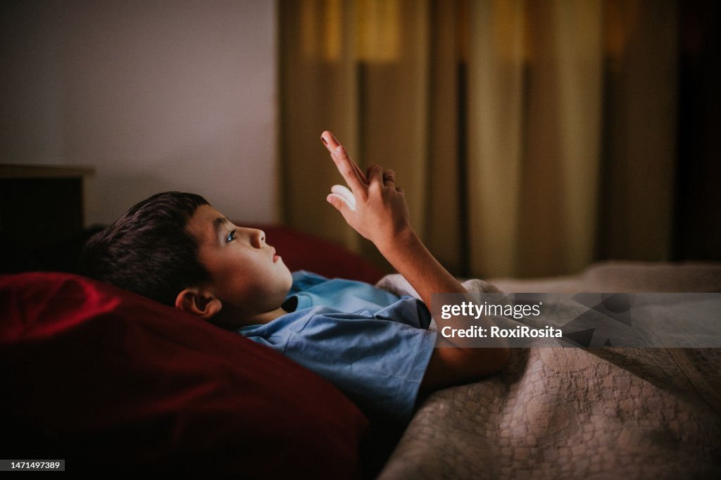 Late-Night Screen Time: Young Boy Lost in His Phone in Bed
