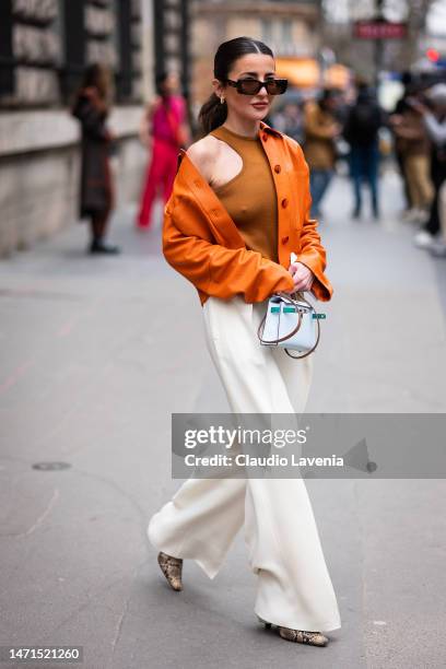 Alexandra Pereira wears a tan tank top, orange leather jacket, cream trousers, snake print boots and Hermes bag, outside Hermes, during Paris Fashion...