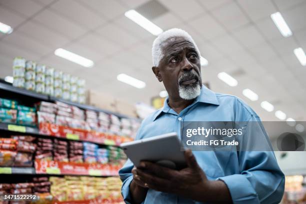 senior man using on the digital tablet in the supermarket - groceries tablet stock pictures, royalty-free photos & images